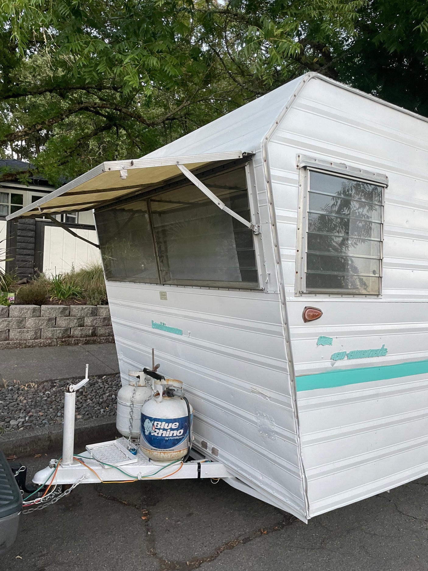White vintage Shasta RV rental with open awning & dual propane tanks, parked outside.