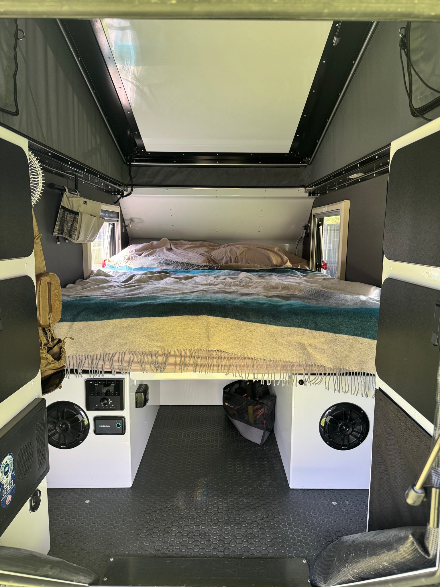 Explore this RV rental's cozy interior: a comfortable bed, control panel, speakers, and practical under-bed storage.