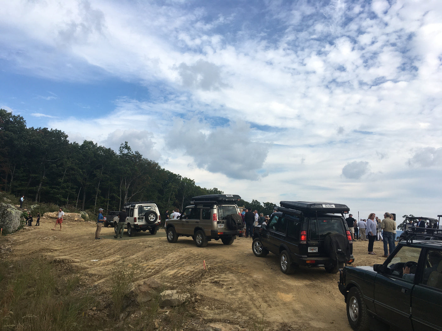Off-road Land Rovers with rooftop tents gather on a dirt trail. Experience outdoor adventures like this with an RV rental!