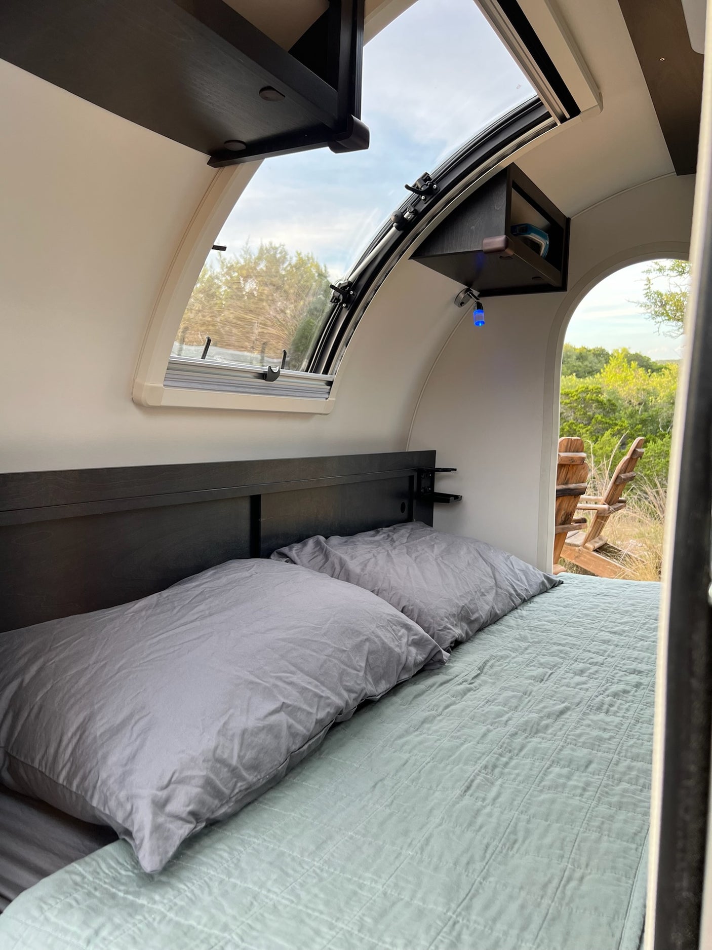 RV rental interior: cozy bedroom with large window, offering an inviting view of nature and outdoor chairs.