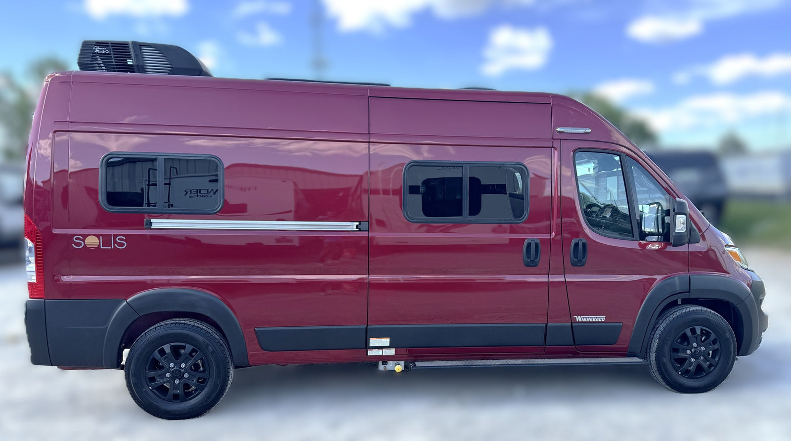A sleek red Winnebago Solis camper van, perfect for an RV rental adventure, parked outdoors on a sunny day.