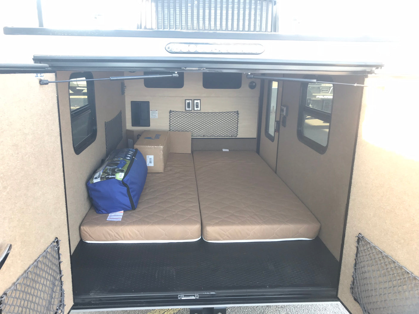 RV rental: Inside a compact camper, featuring two mattresses, side windows, and storage nets on the walls.