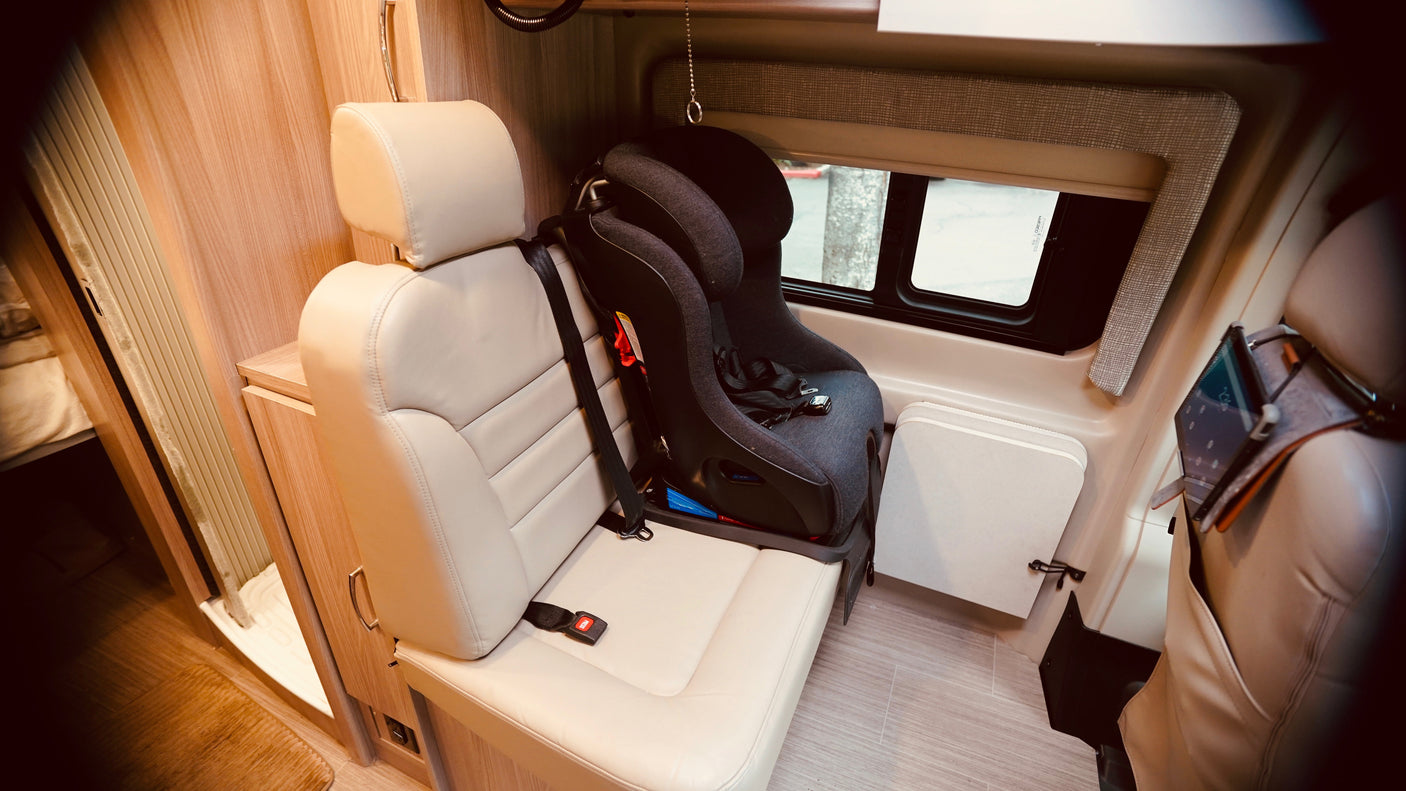 RV rental interior featuring a child safety seat securely installed in a passenger seat, ready for family travel.