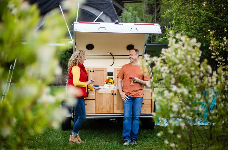 set up on lush grass.|A couple enjoys drinks by their RV rental's outdoor kitchen. This camper provides easy access for glamping and camping adventures.|Family on an RV rental trip: parents relax in a rooftop tent