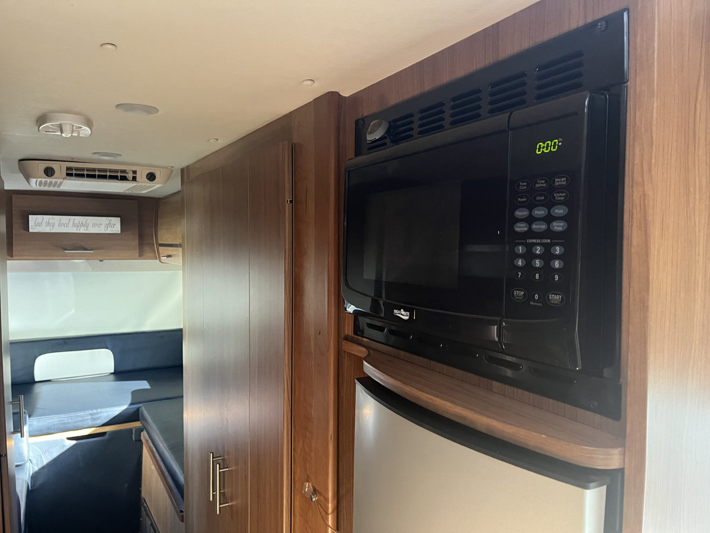RV rental interior: Built-in microwave and fridge surrounded by warm wood cabinetry. Features an AC unit and cozy living space.