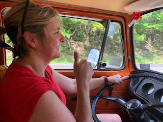 Happy woman gives thumbs up in an orange vintage campervan. Ready for an RV rental road trip adventure!