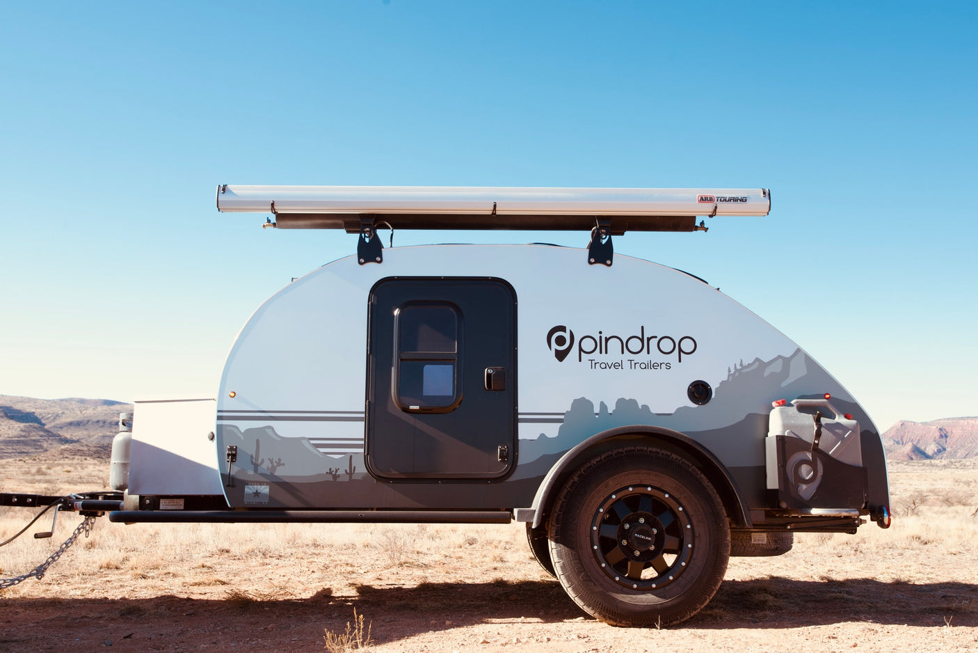 Pindrop teardrop travel trailer, an ideal rv rental for desert adventures, shown with an ARB Touring awning against a blue sky.