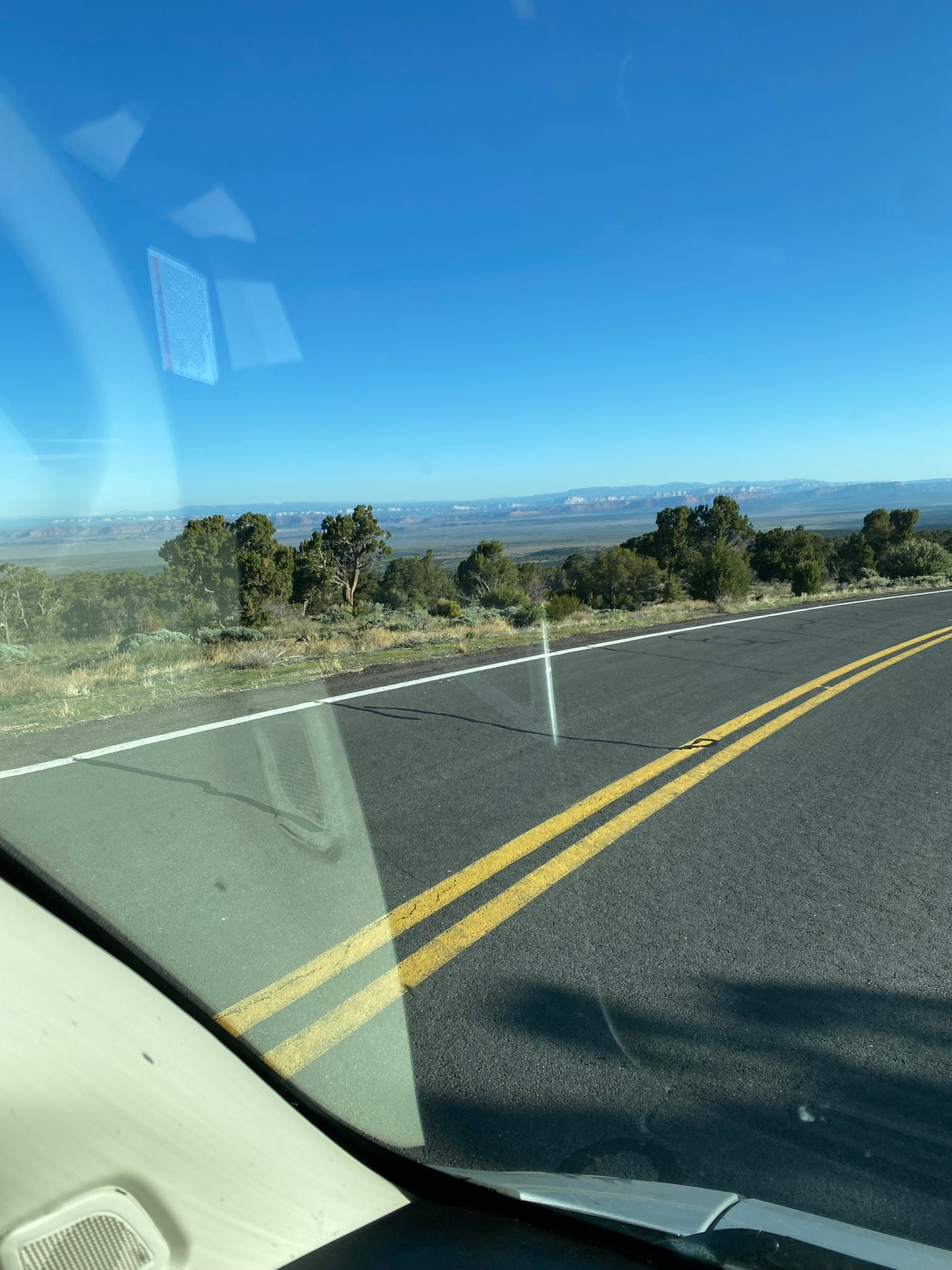 Road trip view from an RV rental: open highway, a distant mountain range, and trees under a clear blue sky.