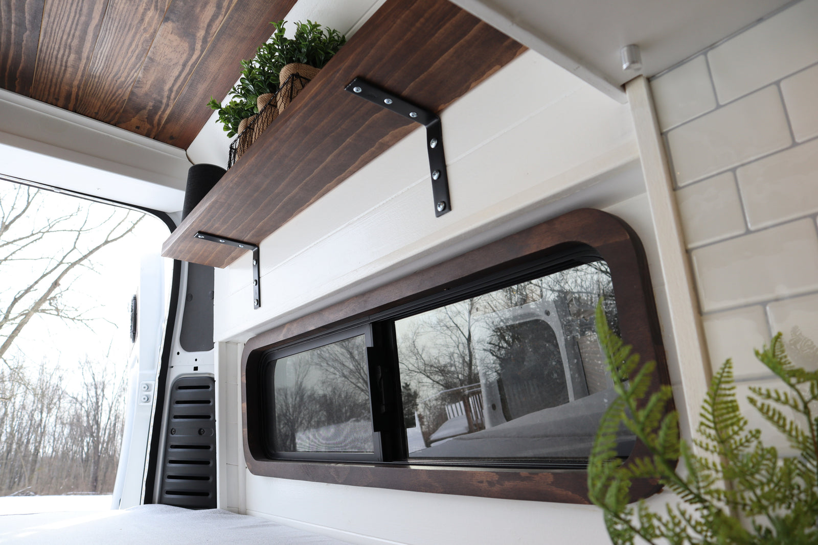 Cozy wood and white camper van rental interior with a custom shelf and snowy window view.