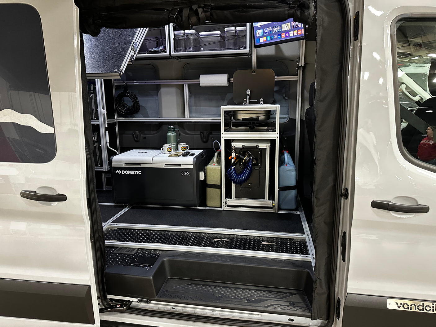 This RV rental shows a fully equipped camper van interior with a Dometic fridge, sink, and TV for mobile living.