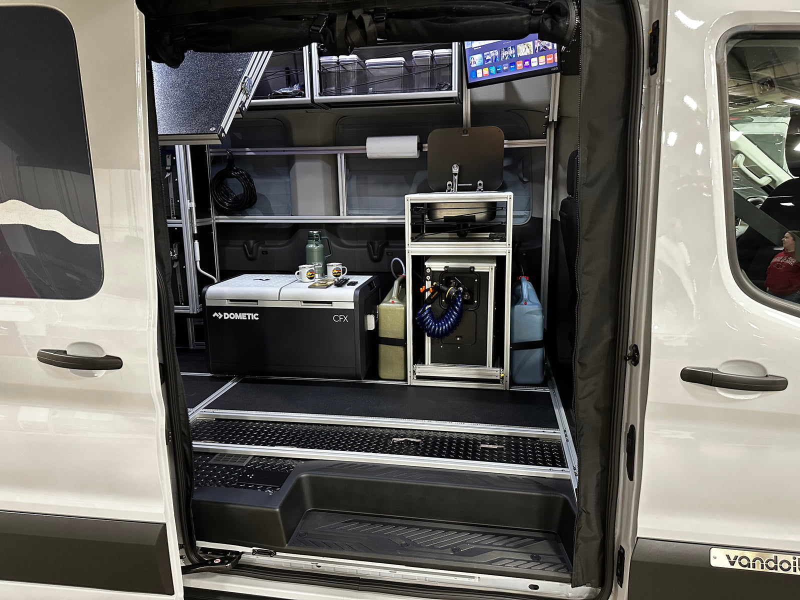 This RV rental shows a fully equipped camper van interior with a Dometic fridge, sink, and TV for mobile living.