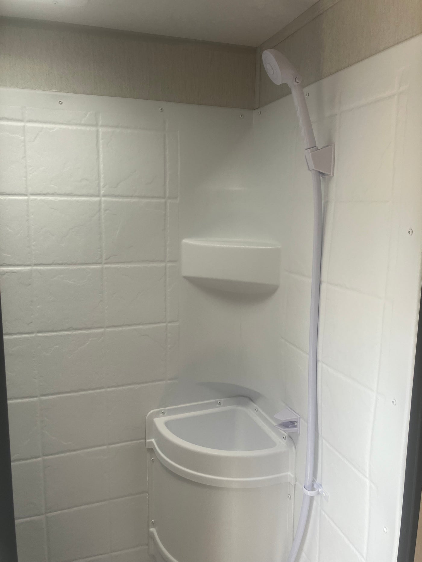 Compact white shower in an RV rental, featuring a handheld shower head, corner shelf, and textured wall panels. — photo 10