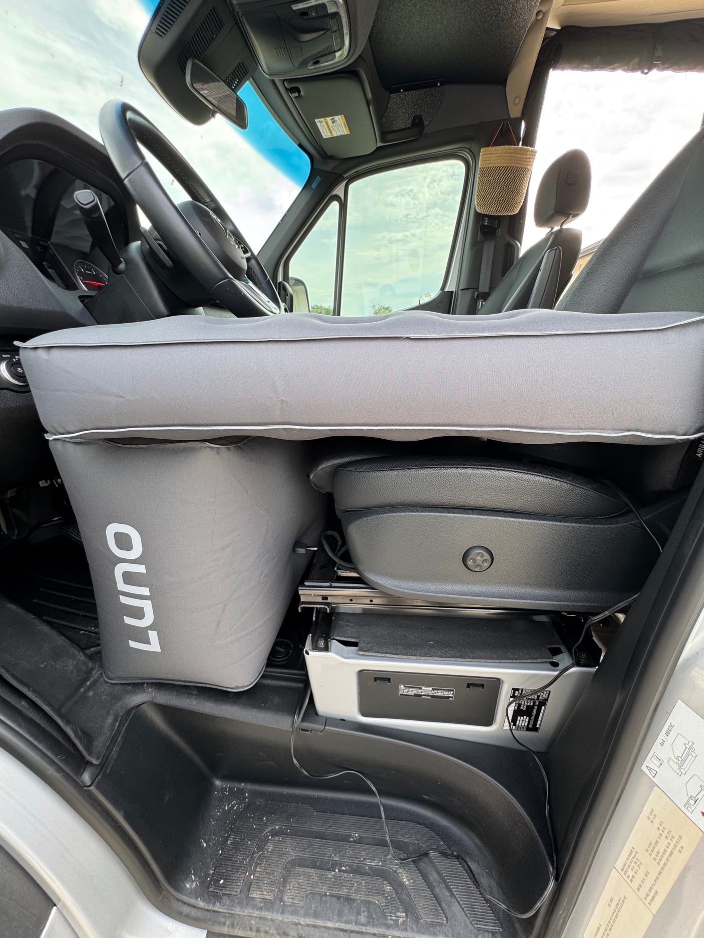 Inside an RV rental: a Luno inflatable mattress spanning the front seats for extra sleeping space, with a portable cooler below.
