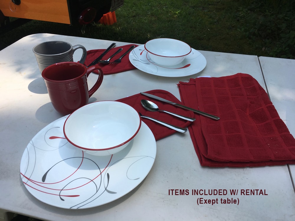 RV rental includes plates, bowls, mugs, cutlery, and towels pictured on a table for easy outdoor dining.