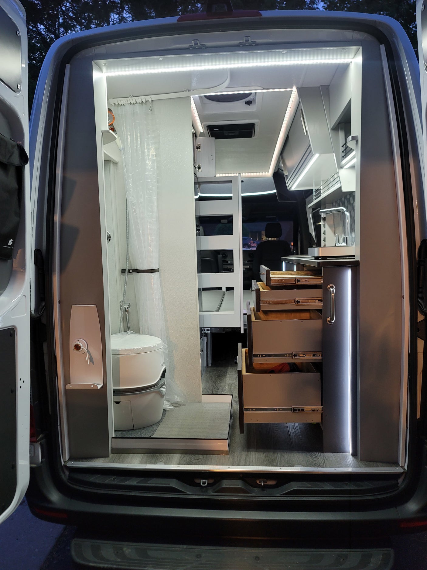 Modern RV rental interior, featuring a compact kitchen, shower, and toilet area, with bright LED lighting.