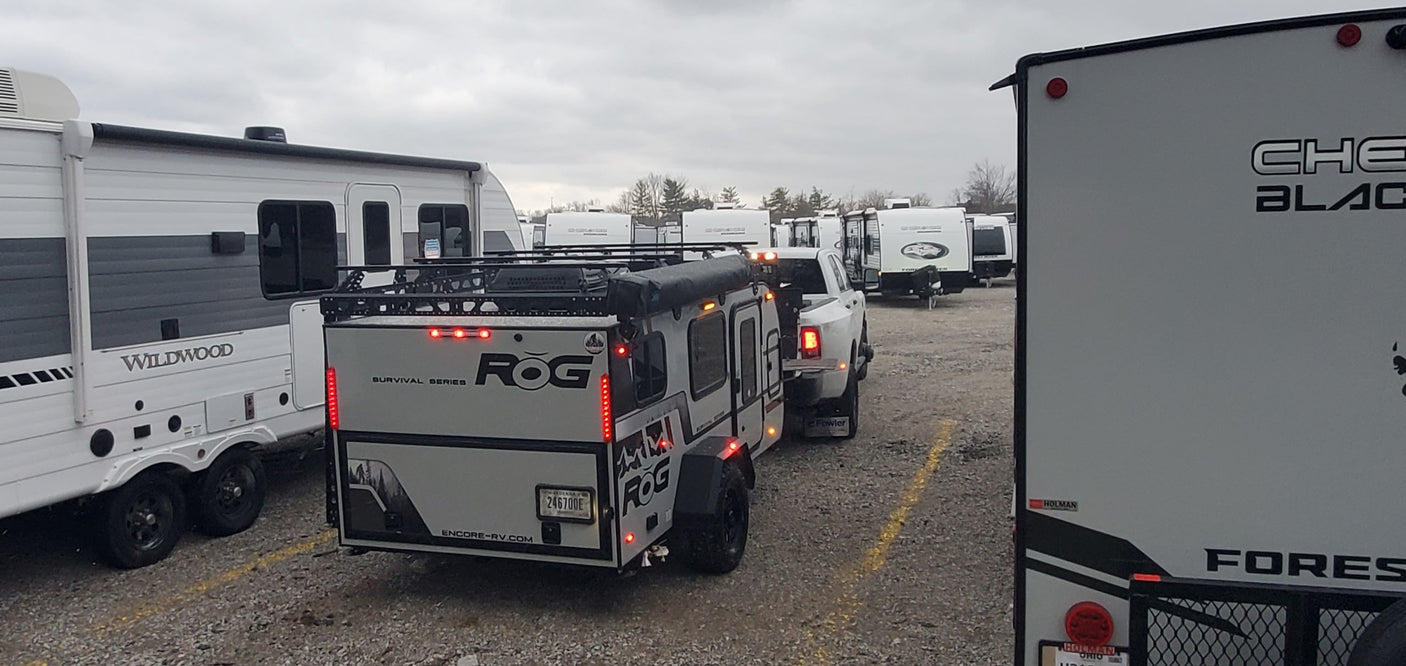 RV rental vehicles: A rugged ROG Survival Series trailer, a Wildwood RV, and others in a storage lot.