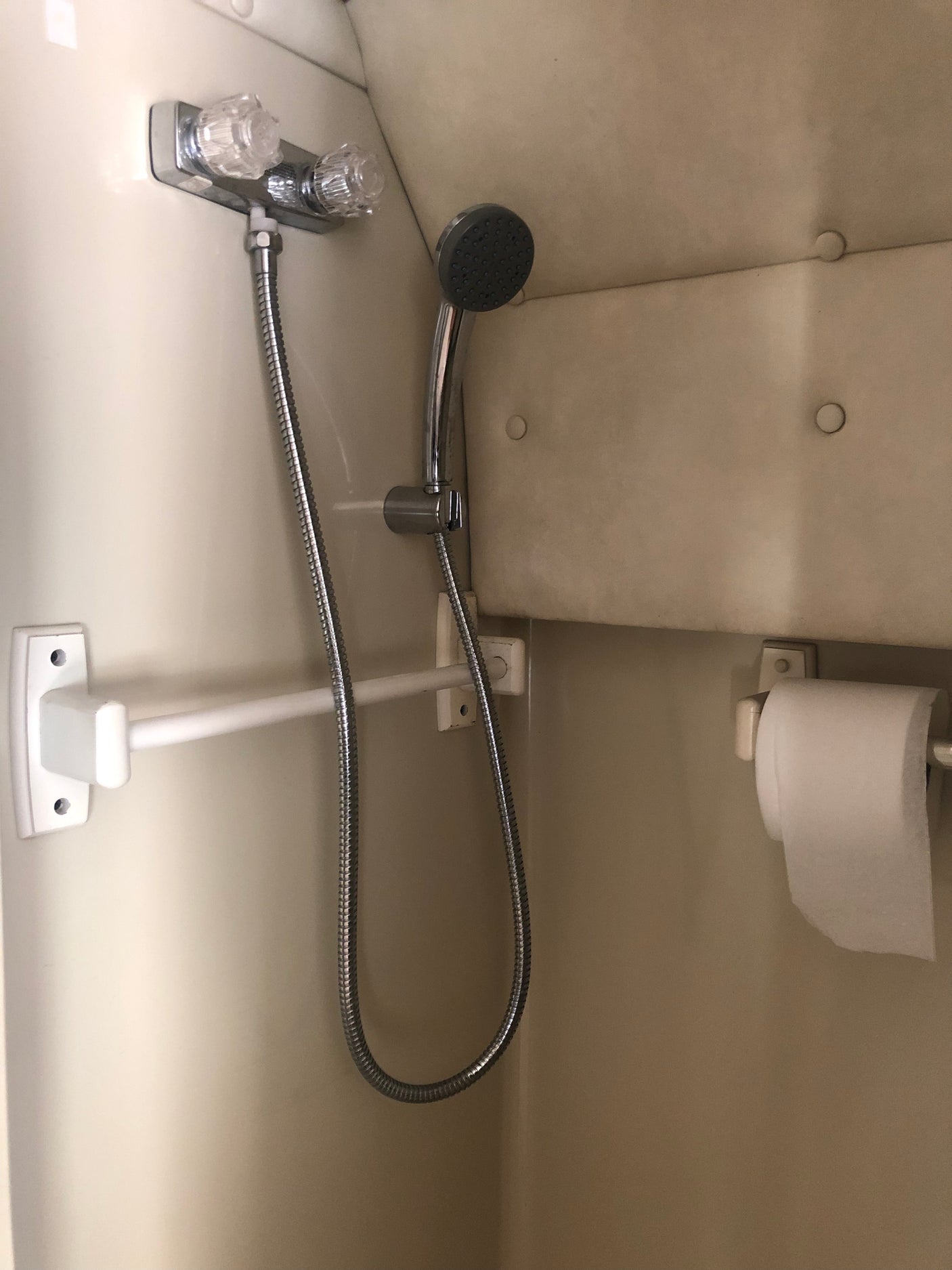 RV rental compact bathroom with a handheld shower, water controls, a white support bar, and a toilet paper holder.