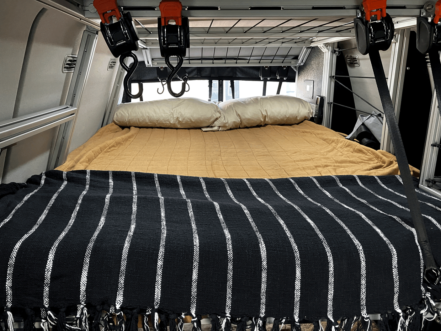 Inside an RV rental: A tidy bed with pillows and a striped blanket, plus handy overhead storage.