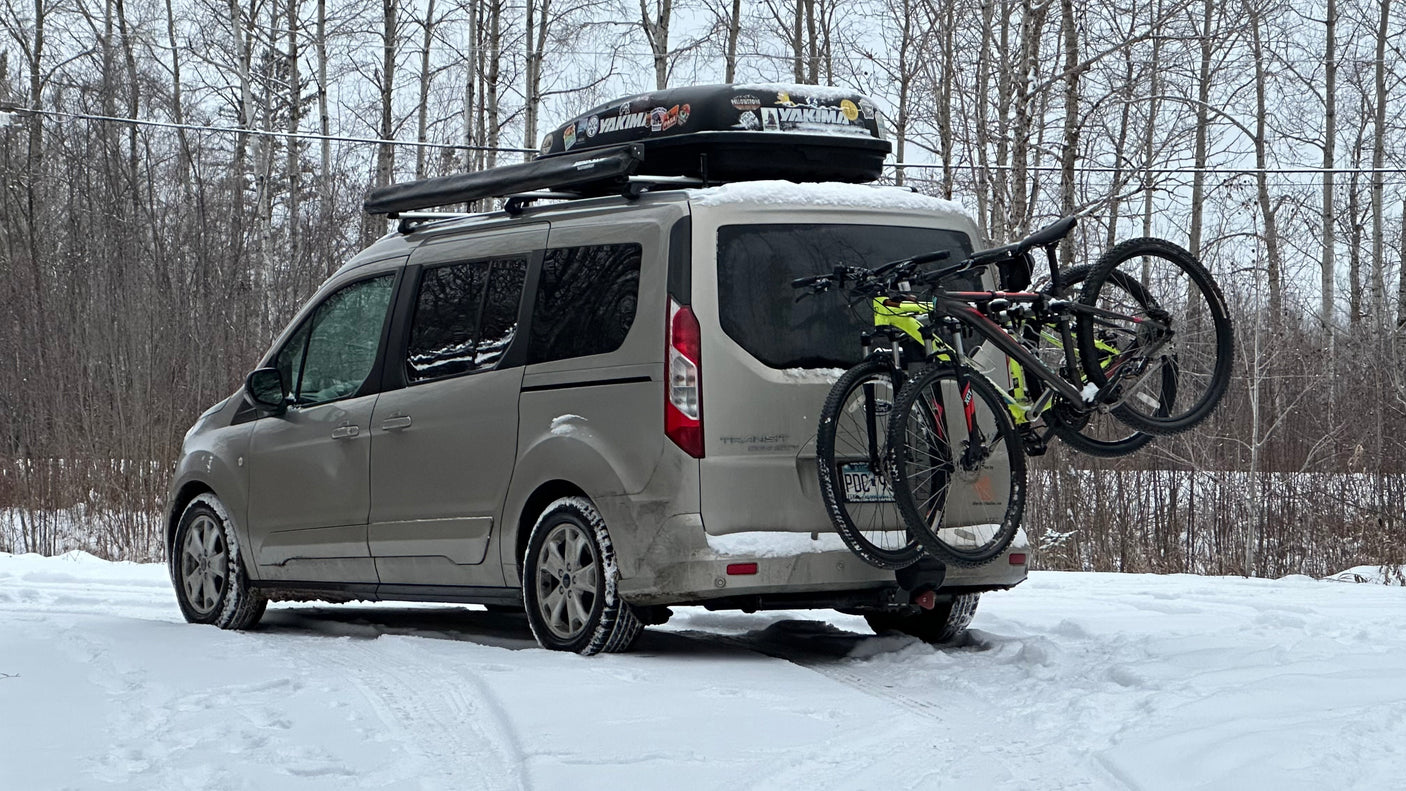 Adventure van in snow: a Ford Transit Connect with bikes, roof box, and an awning. Great for an rv rental trip.