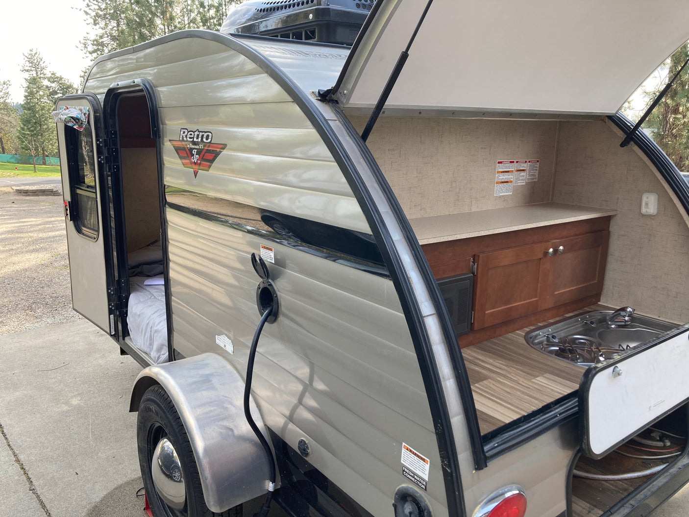 This RV rental teardrop camper features an open side door to a cozy bed and a rear outdoor kitchen with stove and sink.