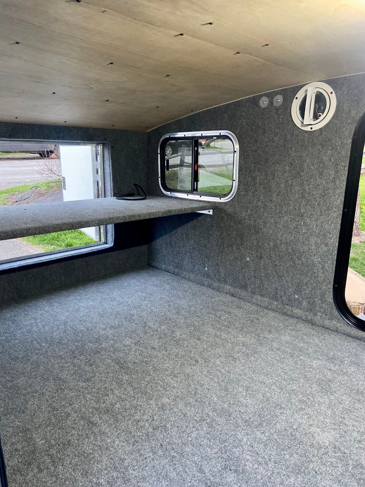 Inside an RV rental: grey carpeted interior, wooden ceiling, windows, and a comfortable raised sleeping platform.