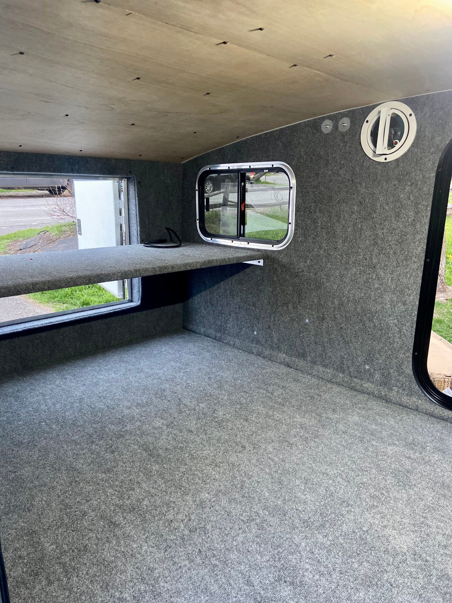 Inside an RV rental: grey carpeted interior, wooden ceiling, windows, and a comfortable raised sleeping platform.