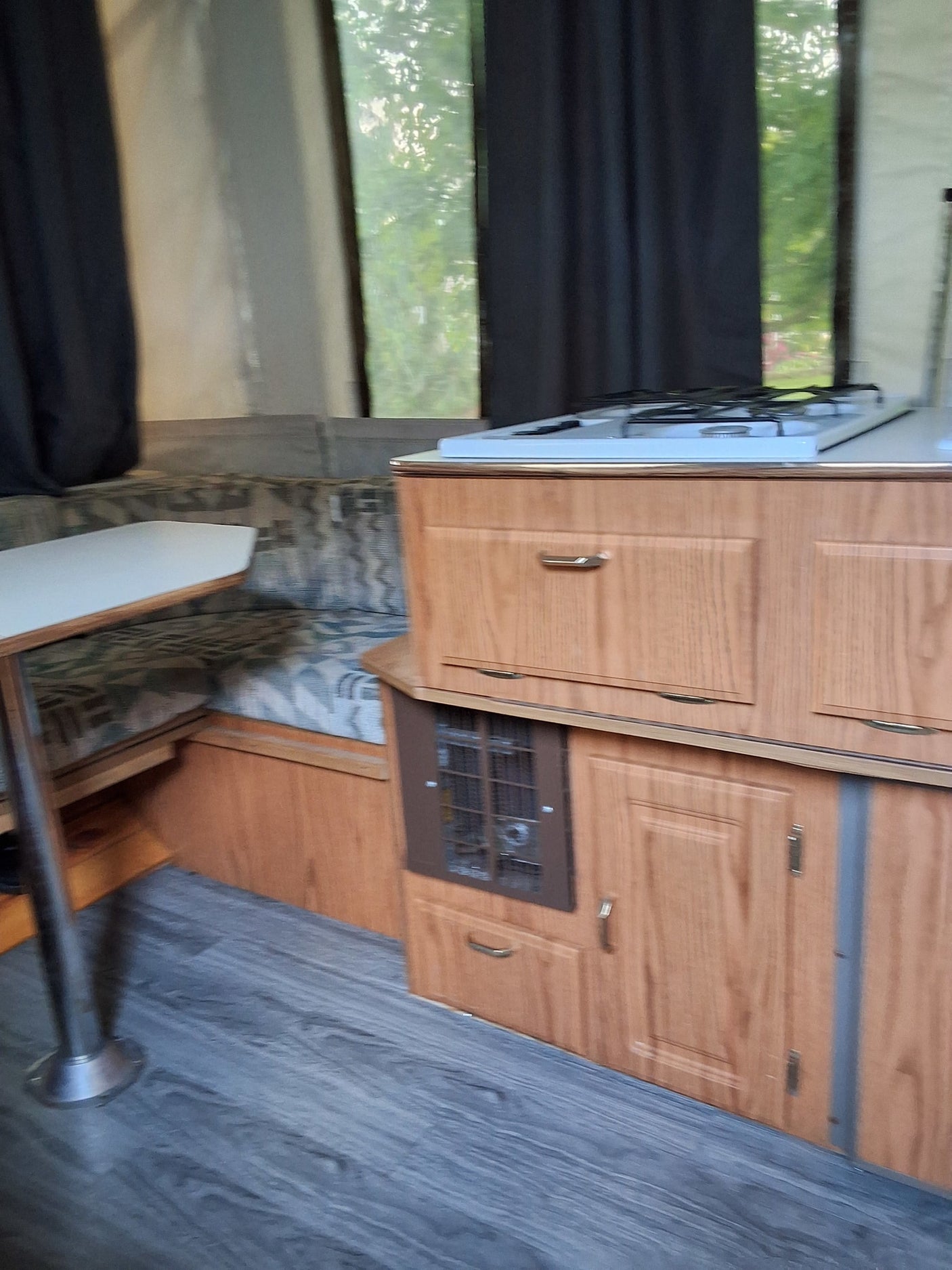Inside an RV rental: a compact pop-up camper kitchen and dinette with wood cabinets and gray flooring.