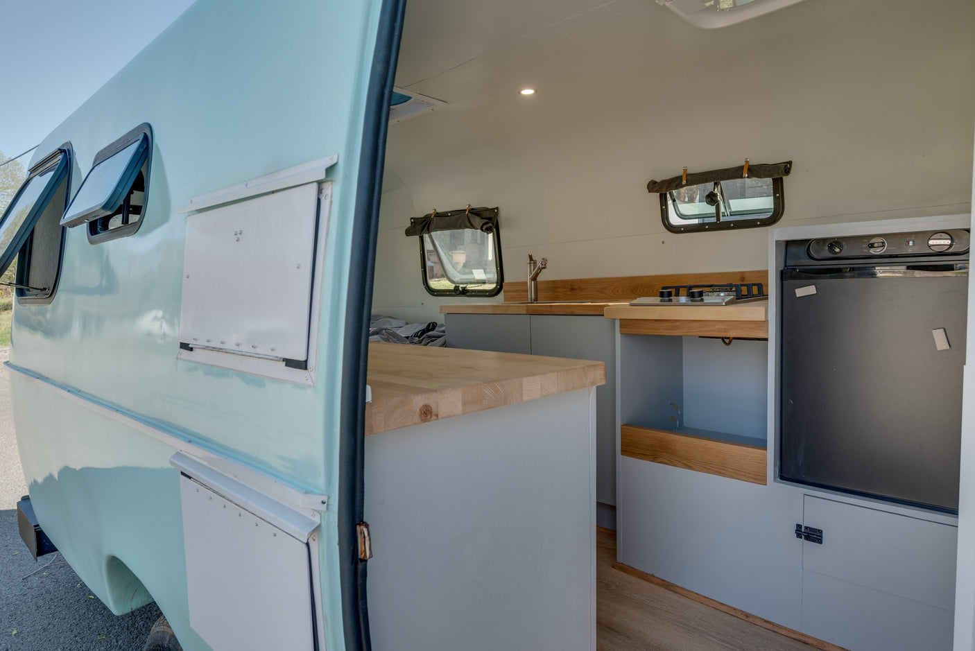RV rental interior: light blue camper with bright kitchen, wood counters, stove, sink, & fridge. Ready for adventures!