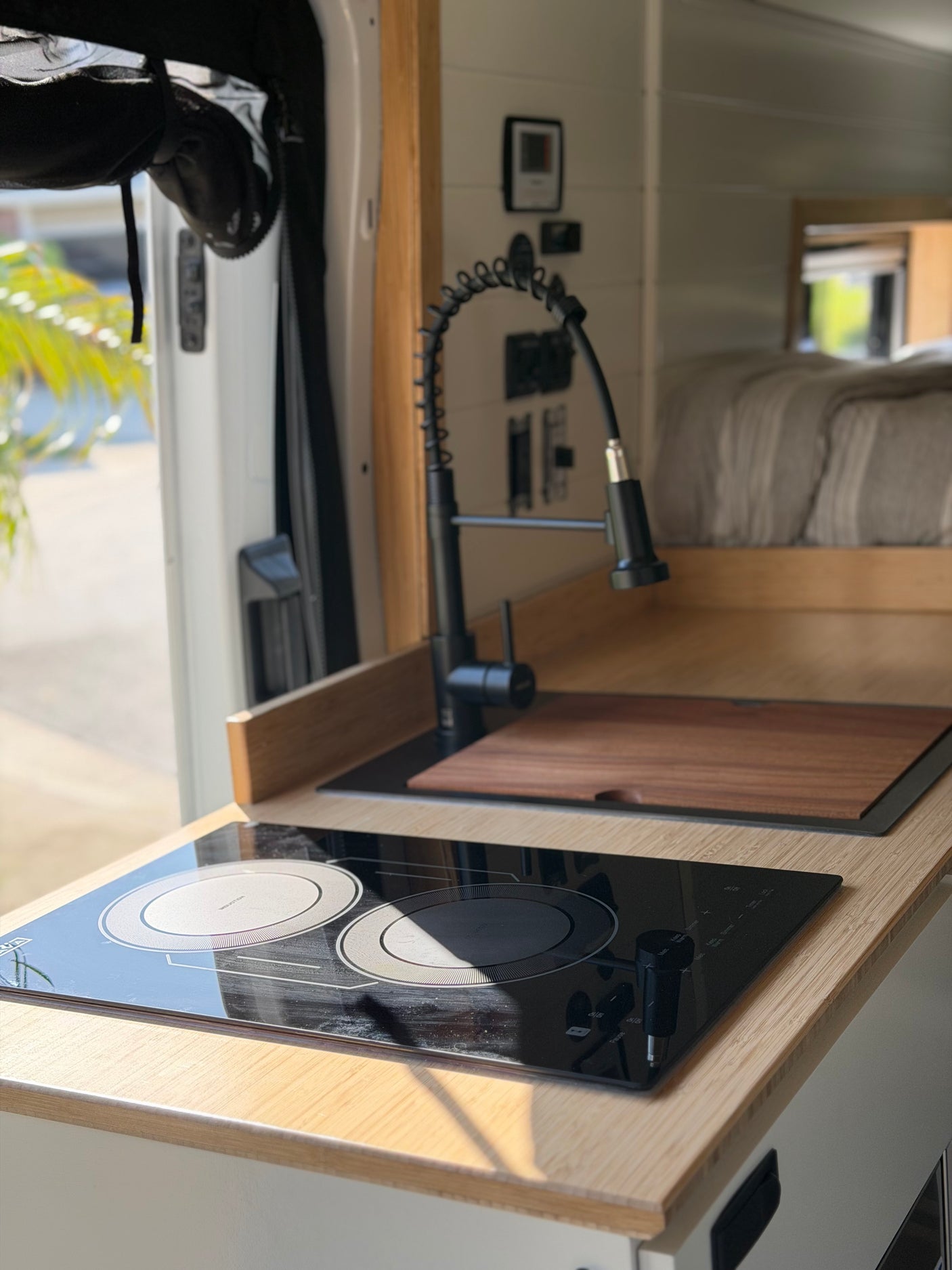 Stylish rv rental kitchen area: two-burner induction cooktop, black faucet, and sink with wooden cutting board.