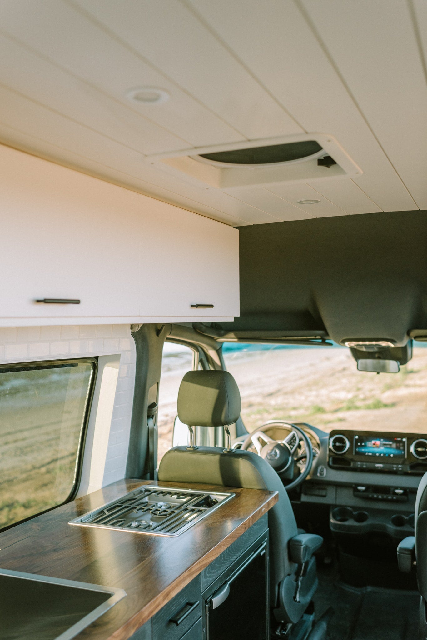 Experience an RV rental! This modern camper van features a full kitchen with stove, sink, wood counters, and driver's area. — photo 6