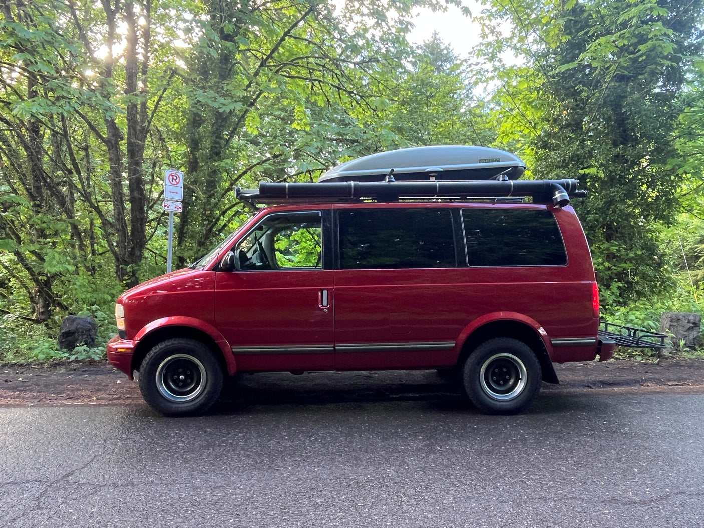 Red van, equipped with a roof cargo box and rear rack, an ideal rv rental for outdoor adventures, parked by a sunny forest.