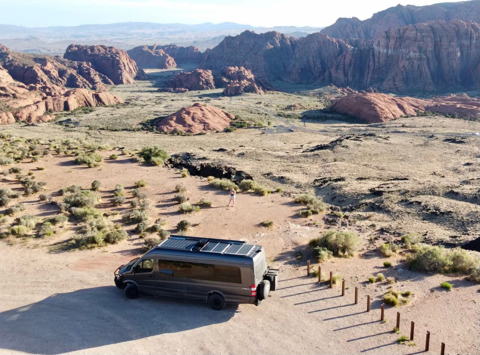with a warm campfire illuminating a large tree. Ideal for outdoor adventures.|RV rental camper van with solar panels parked in a vast red rock desert. A person stands nearby