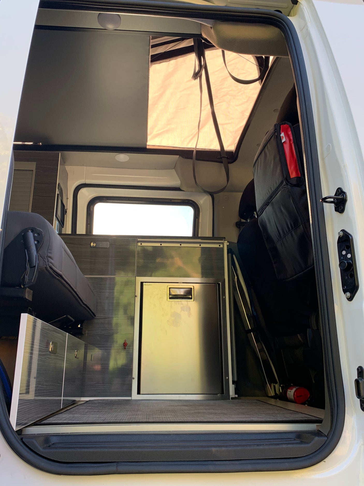 Inside this modern rv rental, see the compact kitchen with fridge, bench seating, and pop-top, viewed from the open door.