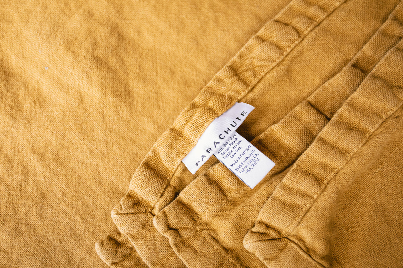 Close-up: textured mustard yellow Parachute bedding with care tag. Perfect comfort for your RV rental travels.