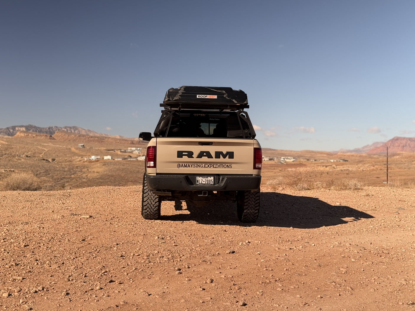 Tan RAM truck with rooftop tent parked on a dirt road in a desert landscape, ideal for an RV rental adventure.
