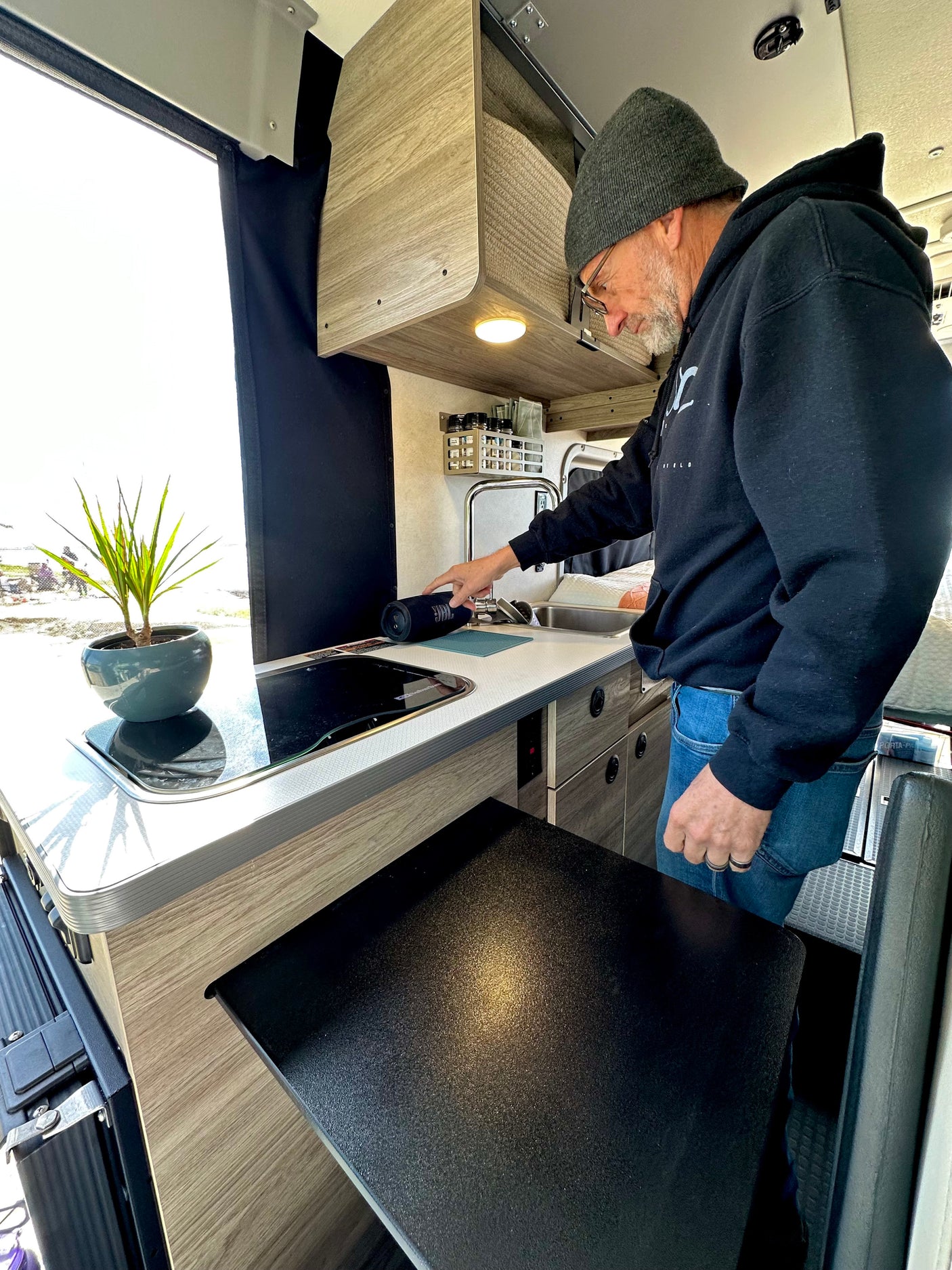 Inside an RV rental: a man operates the compact kitchen, complete with sink, cooktop, and storage, ideal for mobile living.