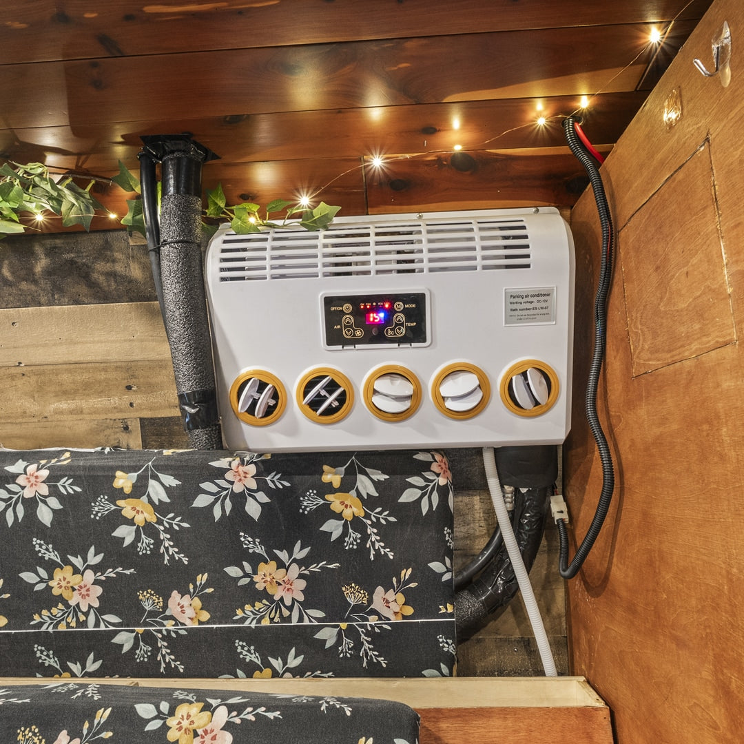 Cool comfort in your RV rental! Interior features a mounted AC unit, floral seating, string lights & wooden accents.