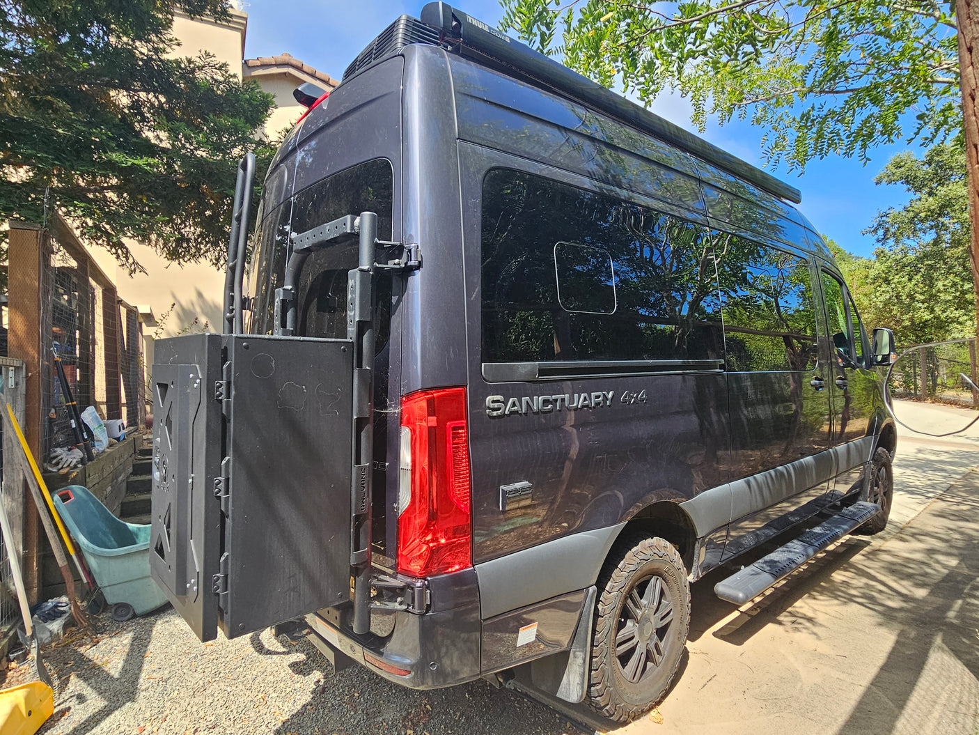 Dark grey Sanctuary 4x4 Mercedes Sprinter van, customized for adventure with rear storage and a roof awning. Great rv rental.