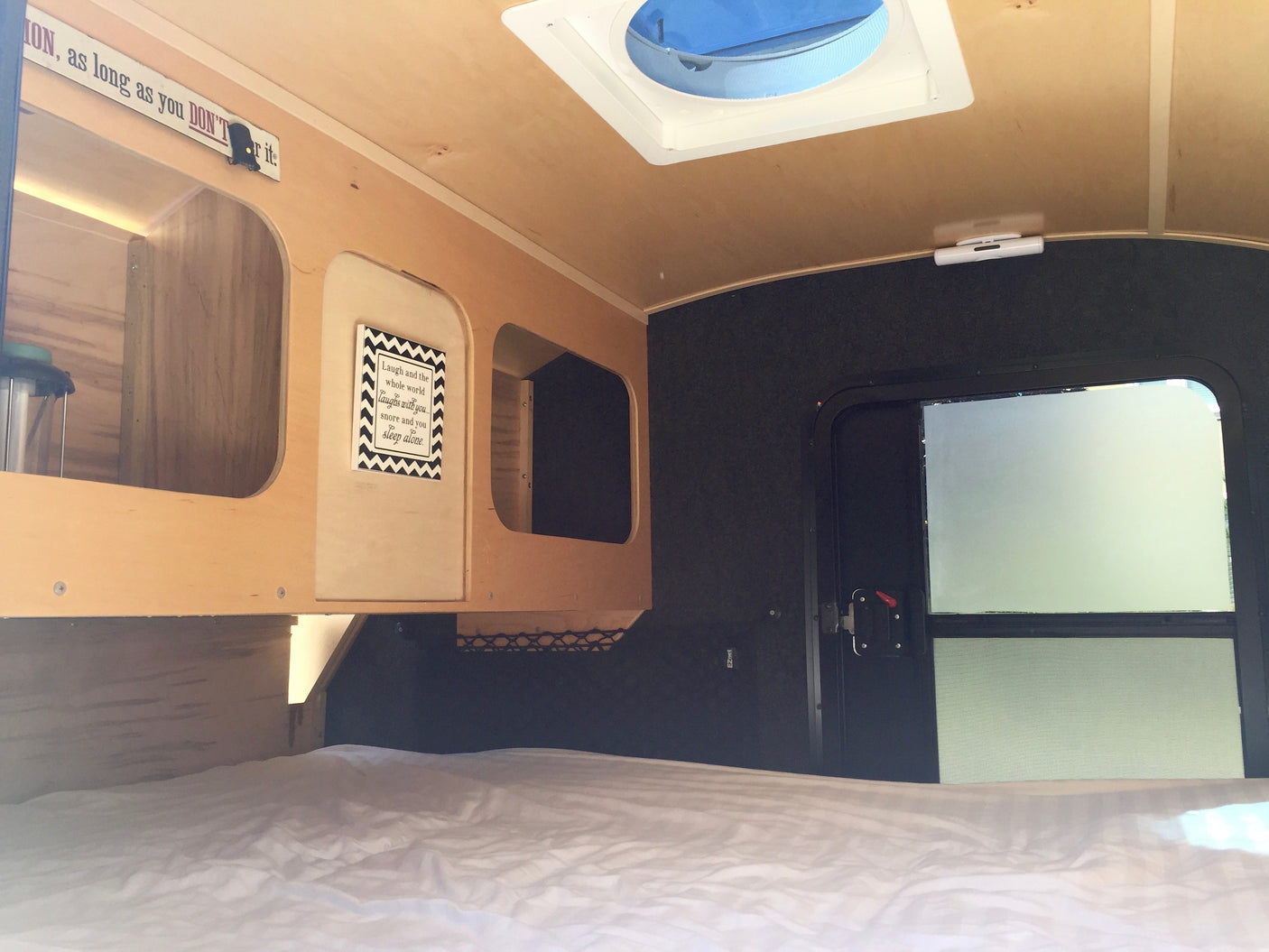 Cozy rv rental interior: bed, built-in wooden storage, ceiling vent, and side door with frosted window.