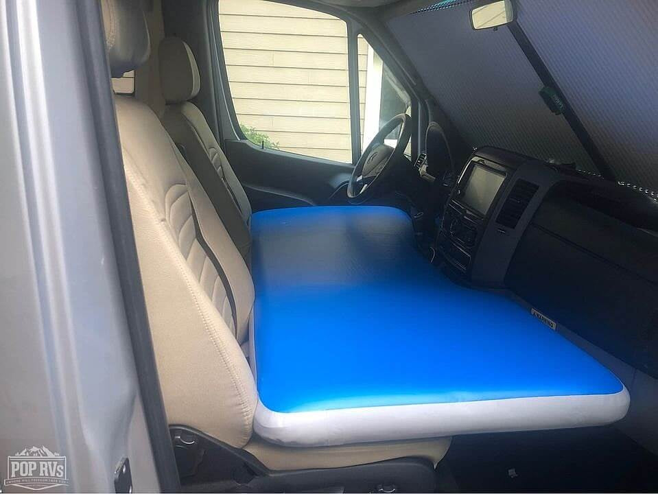Inside an RV rental van, a blue inflatable mattress creates a compact sleeping area across the front seats, ideal for road trips.