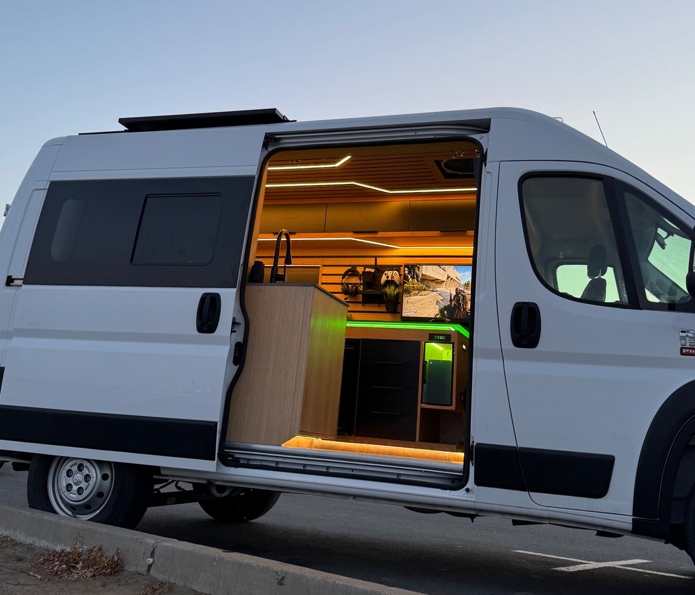 This rv rental showcases a custom camper van with a modern interior, featuring a sink, ambient lighting, and a gaming setup.