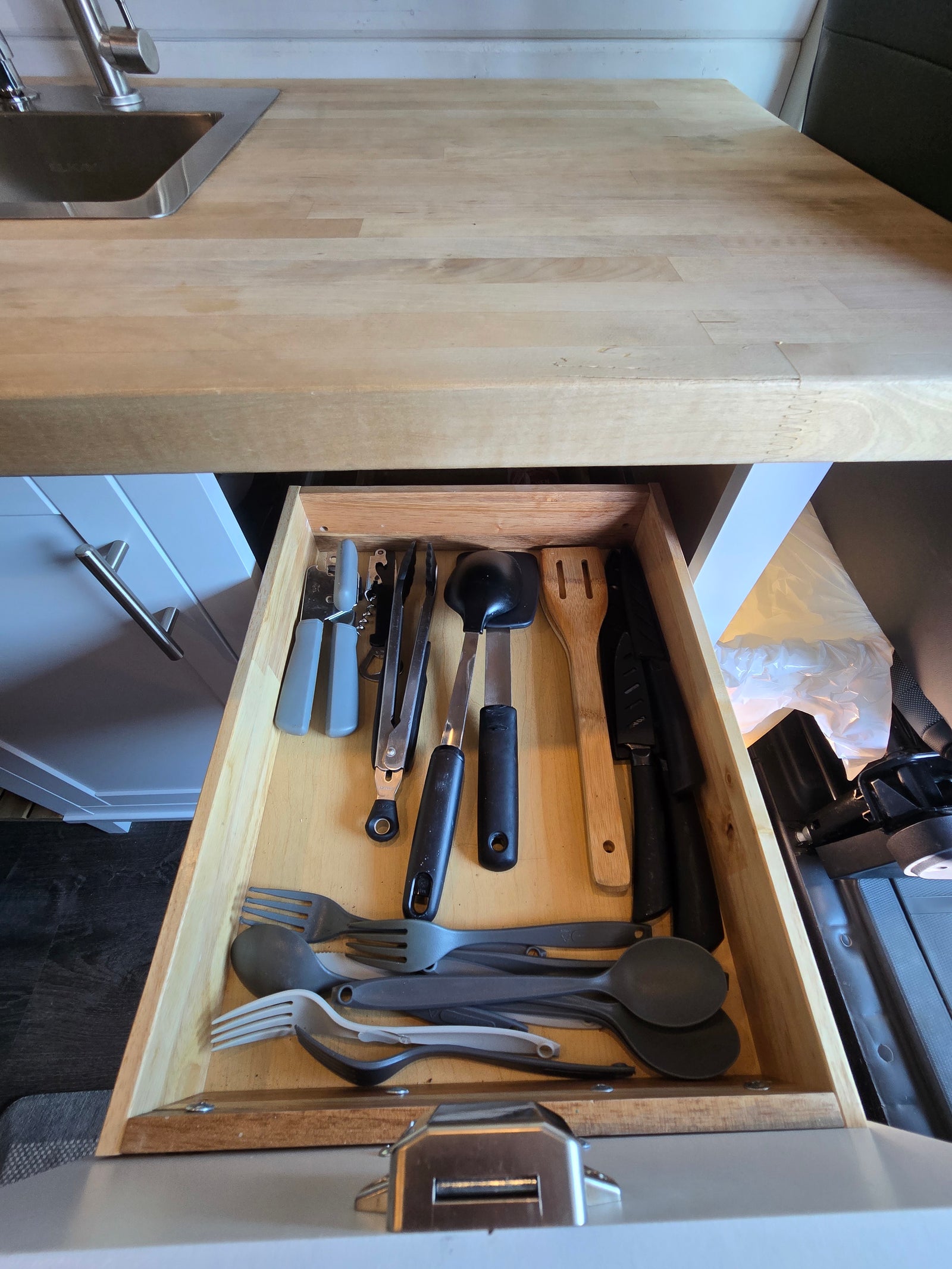 RV rental kitchen's open drawer with neatly stored utensils (forks, spoons, spatulas, knives) and cooking tools.