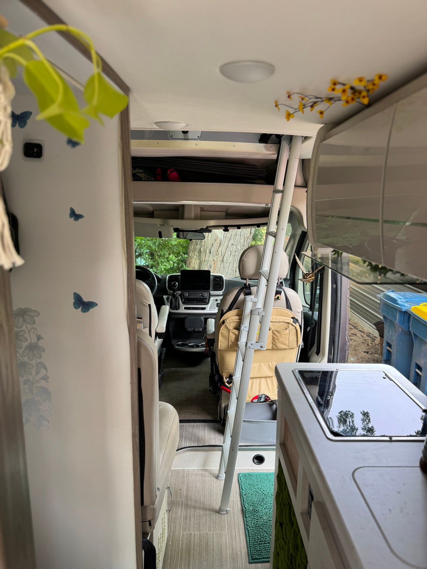 RV rental interior looking forward. Features cockpit, compact kitchen, and ladder. Decorated living space for mobile travel.