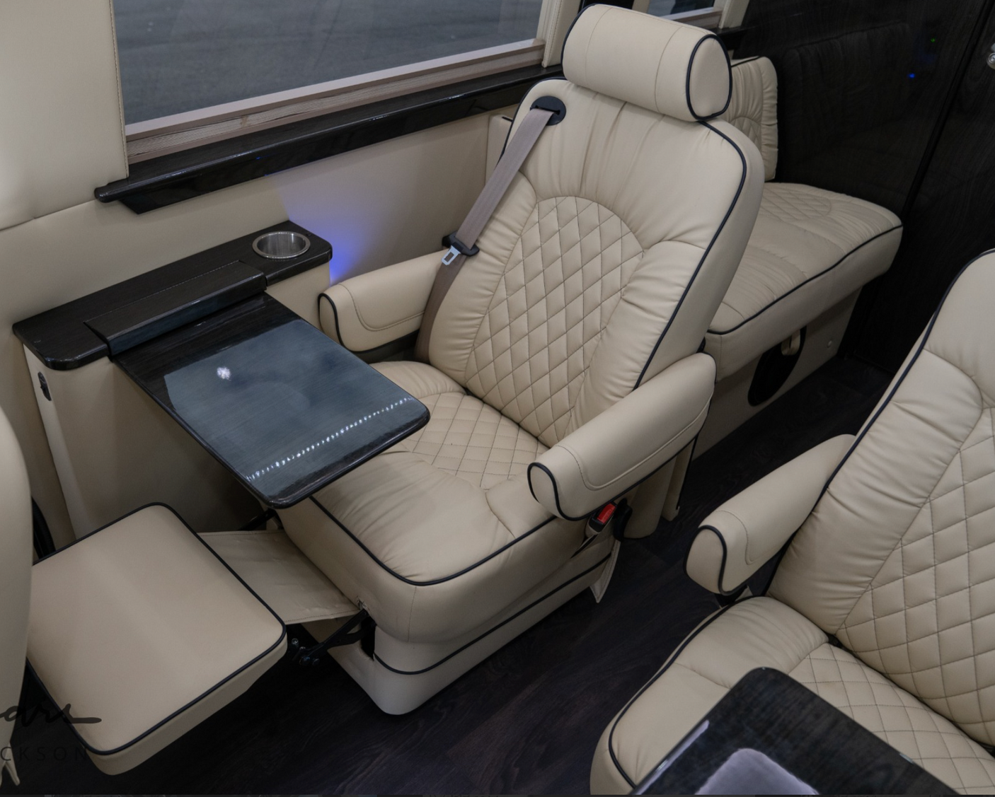 Inside a luxury RV rental: cream leather captain's chairs with a fold-out table and elegant wood trim for comfortable travel.