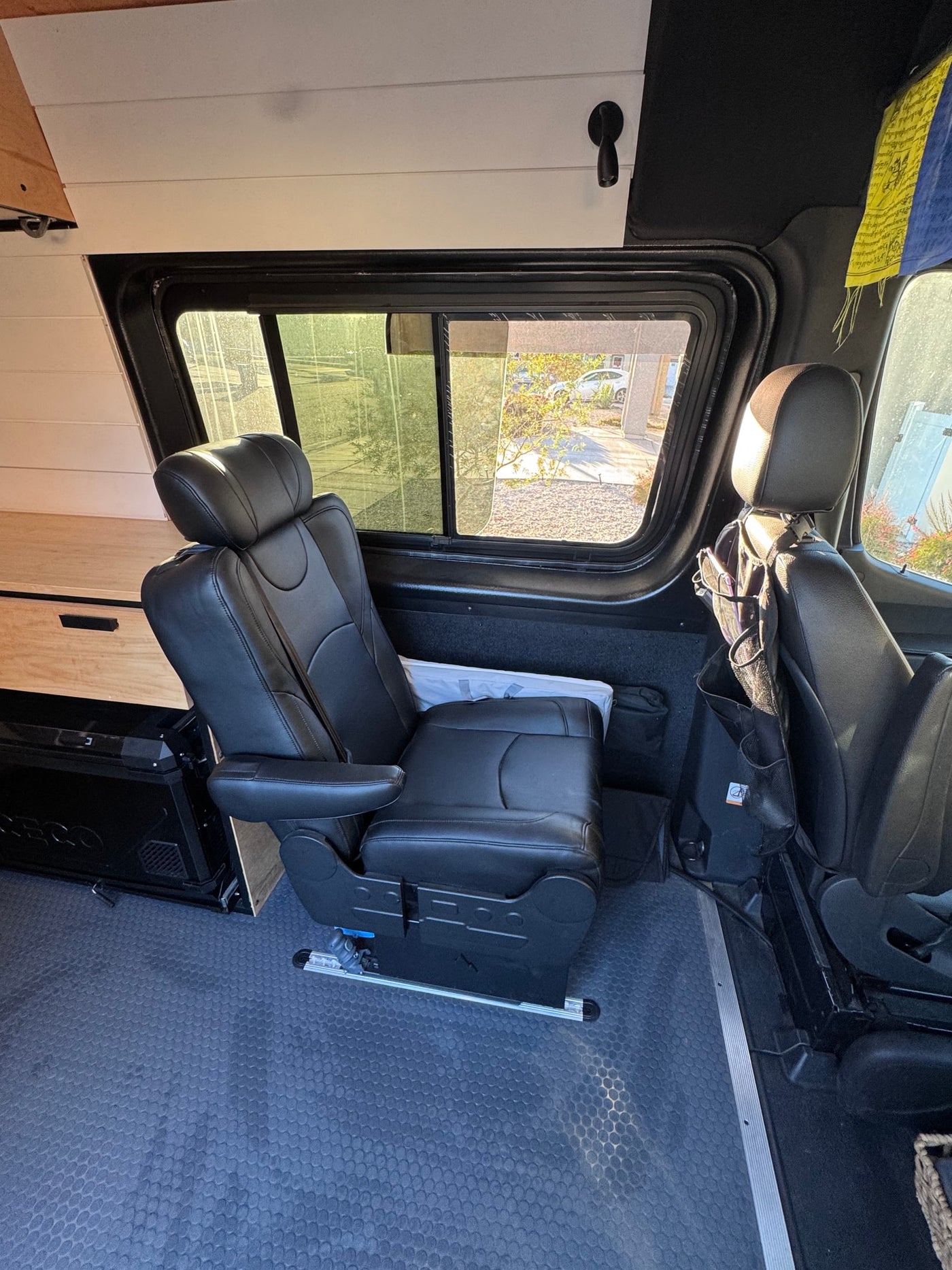 RV rental interior: A black leather captain's chair with armrests, custom wood cabinetry, and large windows in a campervan. — photo 4