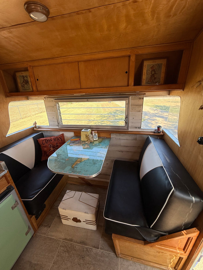 Cozy vintage RV rental dinette featuring black and white benches and a map-themed table, ideal for your next road trip.