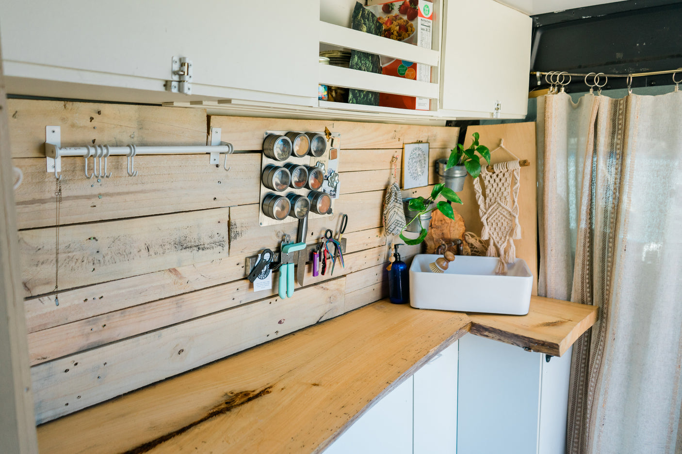 Organized RV rental kitchen interior: wooden backboard, magnetic spice rack, sink, and storage solutions.