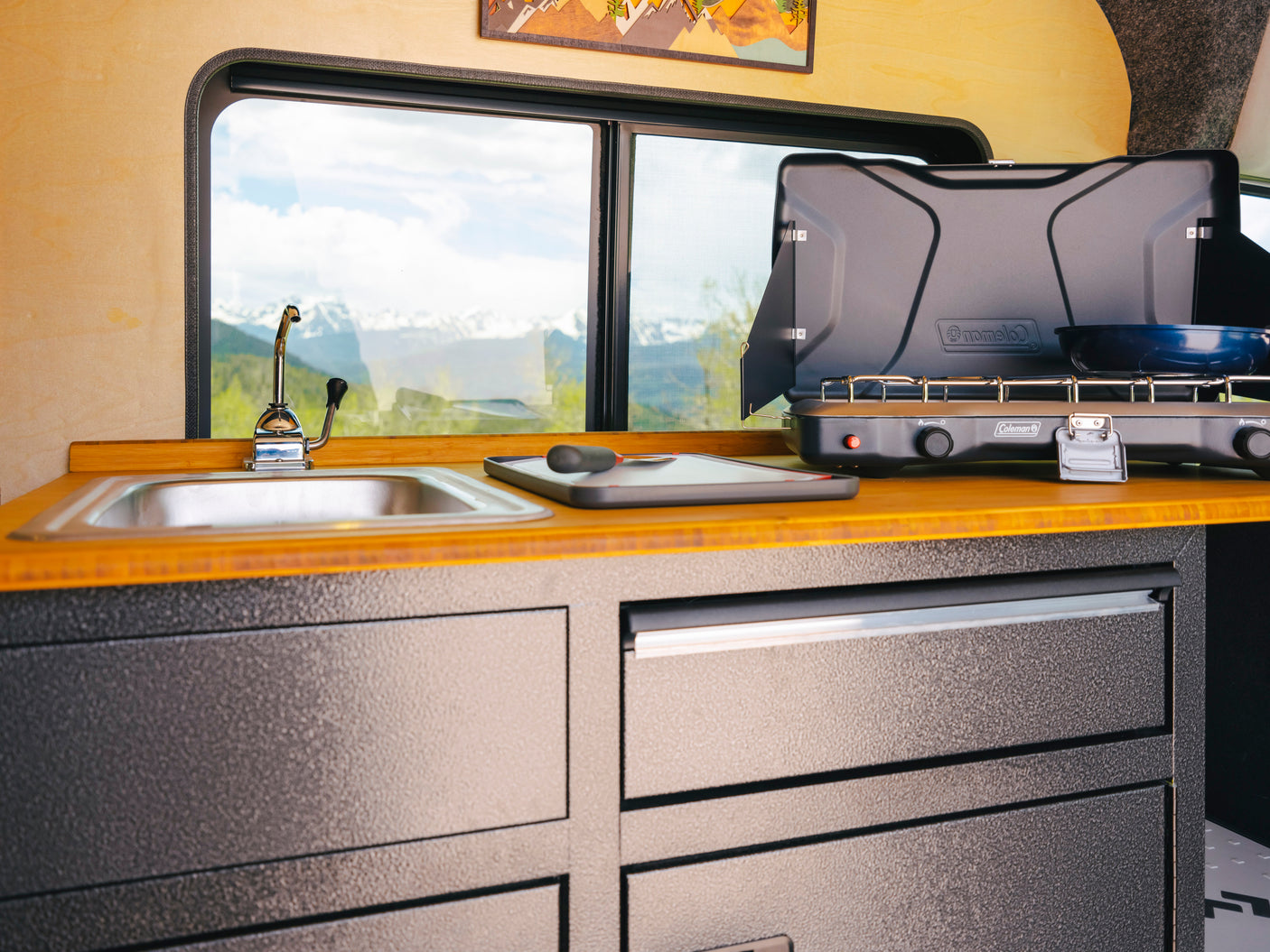 RV rental kitchen: cozy interior with sink, Coleman stove, and stunning mountain views.