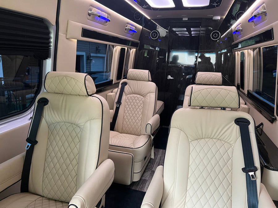 Inside a luxury rv rental: plush cream quilted seats with black trim, blue accent lights, and sleek dark paneling create a lavish cabin.