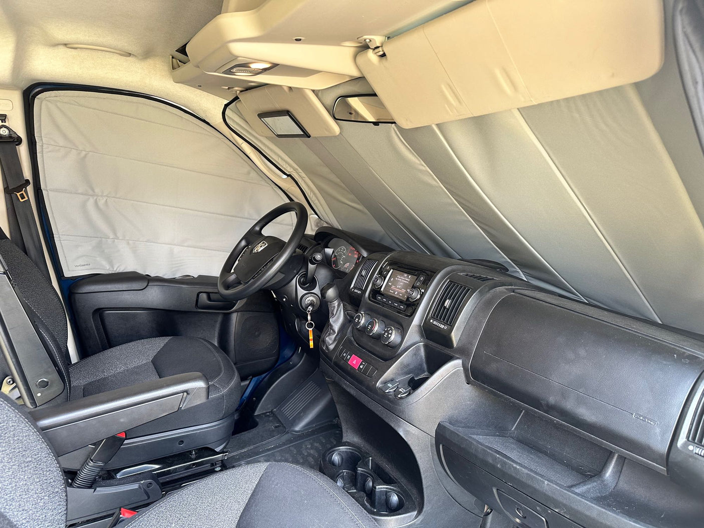 RV rental interior view: cockpit with privacy sunshades on windshield & side windows, dashboard, and front seats.